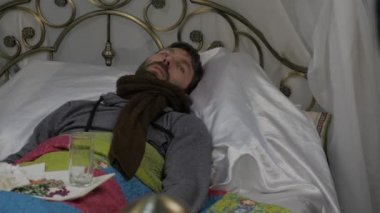 Hasta bir adam sıcak bir eşarp ile bir yatakta boynunu ve bir havlu çevresinde onun baş, video doktor bir dizüstü bilgisayarda sohbet üzerinde yatıyor. 4k