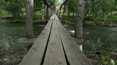 Genç kadın bir dağ nehir üzerinde dar bir ahşap köprü yürüyüş. kamp ve macera kavramı