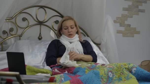 Wanita sakit batuk dan minum pil. Gadis itu terbaring di tempat tidur dengan syal hangat di lehernya. 4K — Stok Video