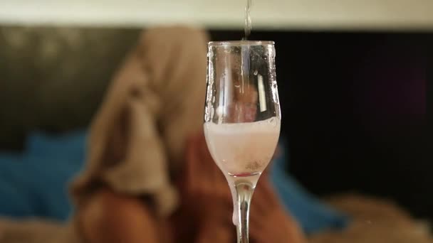 Close-up champagne flows into a glass. Beautiful woman lies on a bed and reads a book. slow motion — Stock Video