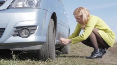 baştan çıkarıcı sarışın kadın çalışırken değişiklik tekerlek üzerinde kırsal yolda bir araba. 4k
