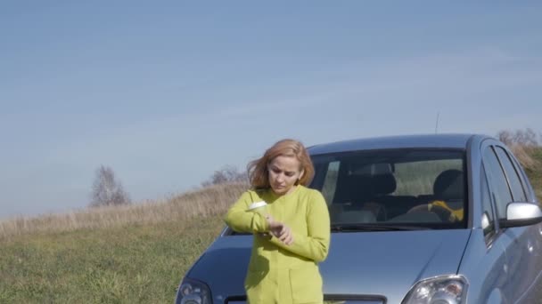 Уверенная молодая деловая женщина с чашкой кофе возле своей машины на сельской дороге. замедленное движение — стоковое видео