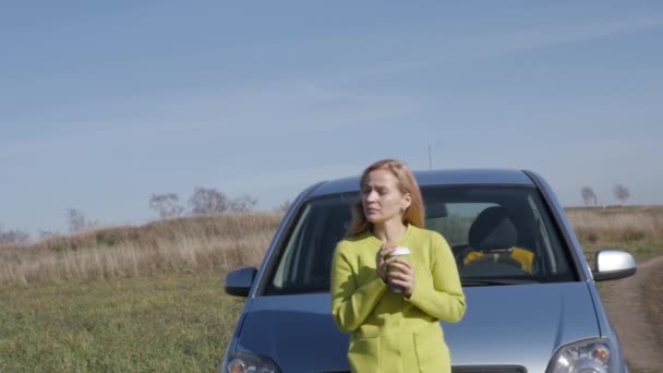 Впевнена молода бізнес-леді з чашкою кави біля її машини на сільській дорозі. повільний рух — стокове відео