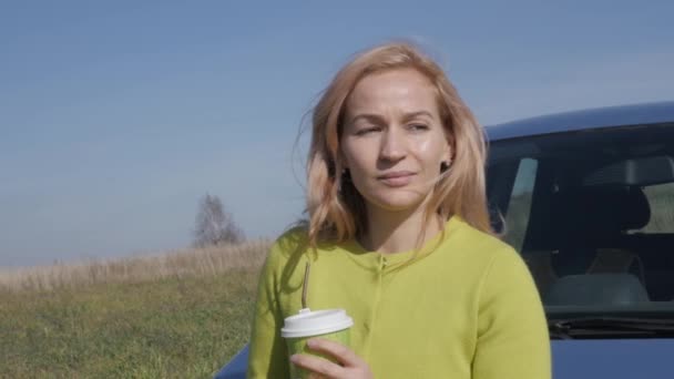 Zeker jonge zakenvrouw met kop koffie in de buurt van haar auto op een landelijke weg. Slow motion — Stockvideo