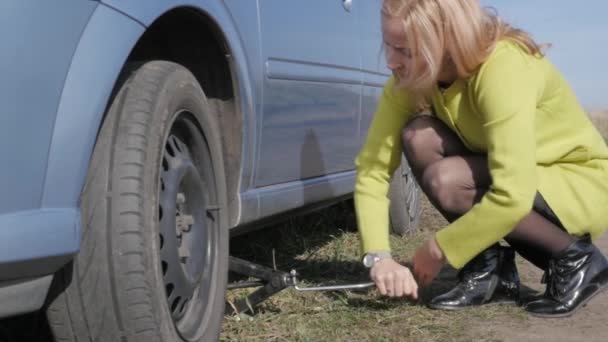Triste charmante jeune femme soulevant voiture cassée avec vis jack sur la route rurale. au ralenti — Video