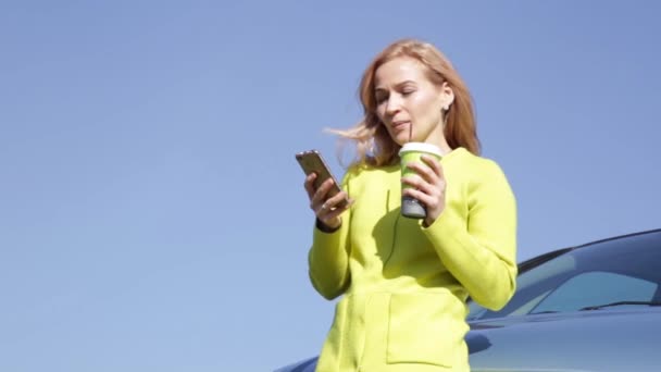 Mujer de negocios joven y segura con una taza de café cerca de su coche está llamando por teléfono móvil . — Vídeo de stock
