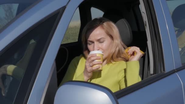 Selbstbewusste junge Frau trinkt Kaffee am Steuer eines Autos. Zeitlupe — Stockvideo