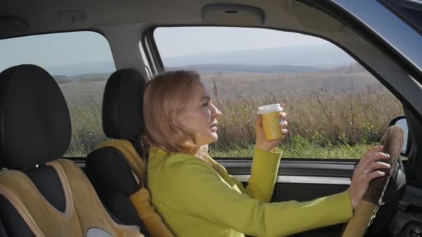 Kendine güvenen genç kadın bir araba direksiyon başında kahve içiyor. ağır çekim — Stok video