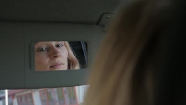 Young glamorous woman is fixing her makeup in a car looking to rearview mirror. slow motion — Stock Video