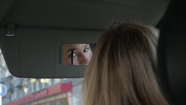 Jonge glamoureuze vrouw verven wenkbrauwen in een auto op zoek naar rearview spiegel. Slow motion — Stockvideo