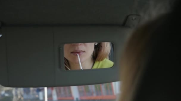 Νεαρή ξανθιά γυναίκα χρωματίζει τα χείλη της στο αυτοκίνητο ψάχνει να καθρέφτη. αργή κίνηση — Αρχείο Βίντεο