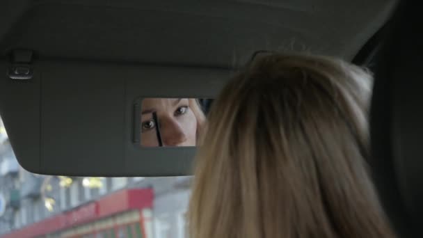 Jonge glamoureuze vrouw verven wenkbrauwen in een auto op zoek naar rearview spiegel. Slow motion — Stockvideo