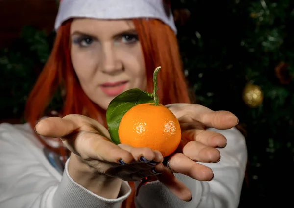 Young redhead woman holding tangerine on a Christmas decorations background. concepte of waiting Christmas and New Year