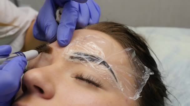 Close-up van de handen van de meester doet wenkbrauwen tatoeage. permanente wenkbrauw make-up. Slow motion — Stockvideo