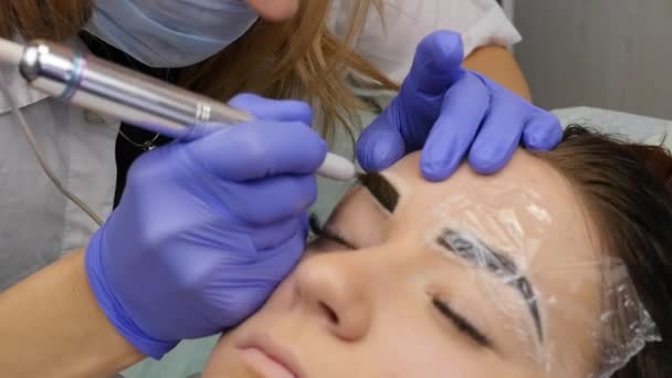 Mujer hermosa joven conseguir tatuaje de las cejas. maquillaje permanente para las cejas en el salón de belleza. cámara lenta — Vídeos de Stock