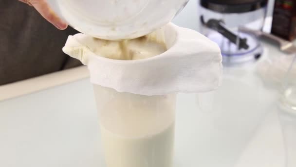Руки молодой женщины, выдавливающей органическое молоко из мешка или сырной ткани. Концепция здорового питания — стоковое видео