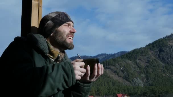 Hombre barbudo solitario de pie en la cubierta de observación mirando a una montaña y beber café o té de la taza grande. cámara lenta — Vídeo de stock