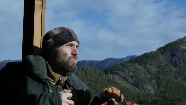 Hombre barbudo solitario de pie en la cubierta de observación mirando a una montaña y beber café o té de la taza grande. cámara lenta — Vídeo de stock