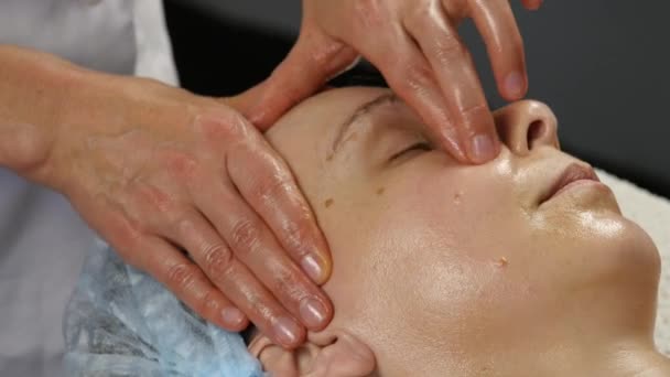 Ärztin macht Anti-Aging-Massage für den Kunden. Frau genießt Plastik-Gesichtsmassage in Wellness-Satin. 4k — Stockvideo