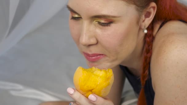 Rusovláska žena jí čerstvé ovoce vleže v posteli. Zdravá snídaně. Zpomalený pohyb — Stock video