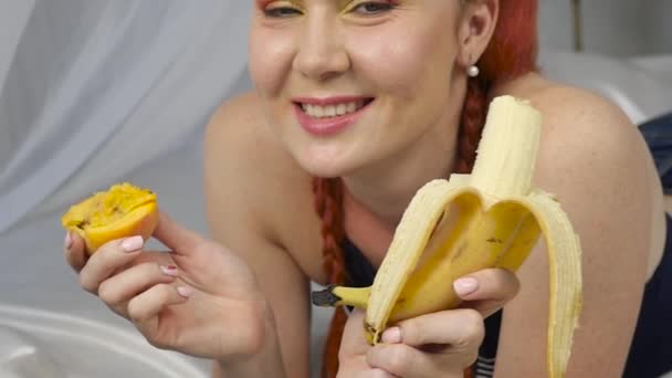 Roodharige vrouw eet vers fruit terwijl liggend in bed. gezond ontbijt. Slow motion — Stockvideo