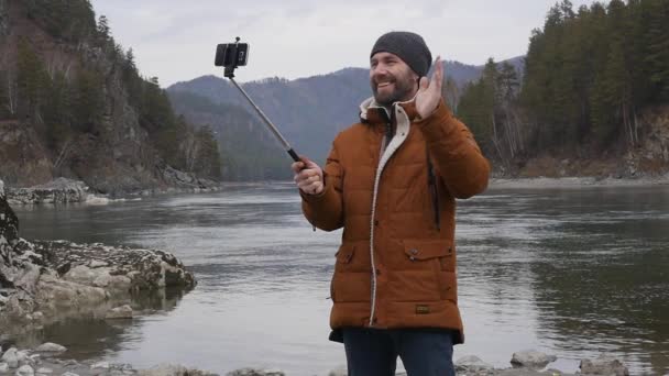 Bebaarde toeristische foto's zelf op een mobiele telefoon op de oever van een rivier berg. Slow motion — Stockvideo