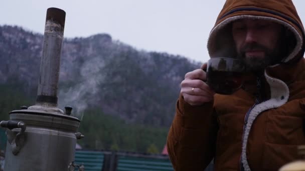 Бородач пьет чай в туристическом лагере в горной долине. Путешествие в холодное время года как образ жизни. замедленное движение — стоковое видео