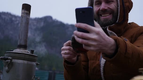 Bearded man is drinking tea in tourist camp in the mountain valley. Travel in the cold season as a lifestyle. slow motion — Stock Video