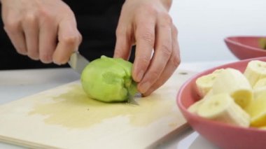Kadın mutfaktaki tahta bir tahtayla kiviyi kesti.