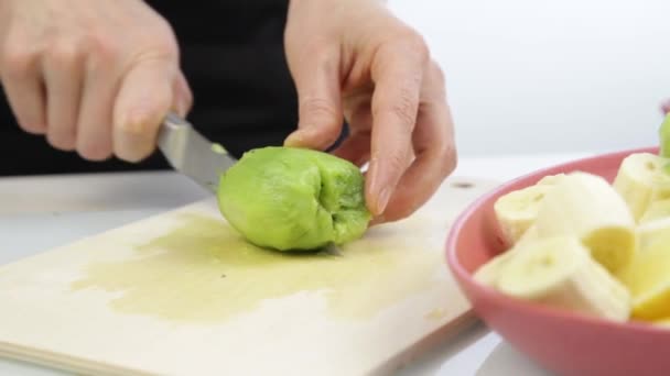 Woman cut the kiwi on a wooden board in the kitchen. — Stock Video