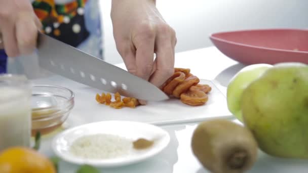 Руки режут сушеные абрикосы большим ножом на доске. приготовление здоровой пищи — стоковое видео
