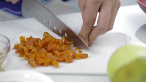 Handen hakken gedroogde abrikozen met grote mes op de snijplank. Koken gezond voedsel — Stockvideo