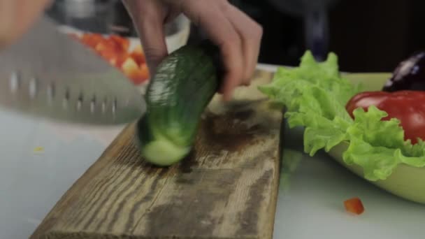 女性は、台所のテーブルにサラダにキュウリをスライスします。木製のまな板でカット野菜. — ストック動画