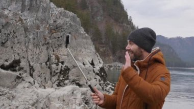 sakallı turist video konferans bir cep telefonu üzerinde arkadaşlarınızla bir dağ nehir kıyısında yaşıyor. ağır çekim