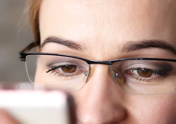 Close-up bruine vrouw oog in glazen. Vrouw met behulp van een smartphone — Stockfoto