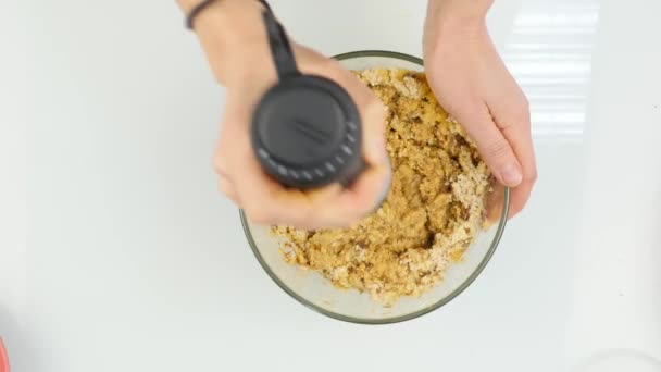 Mujer mezcla frutos secos con frutas secas en un recipiente de vidrio. cocinar alimentos saludables. vista superior 4K — Vídeos de Stock