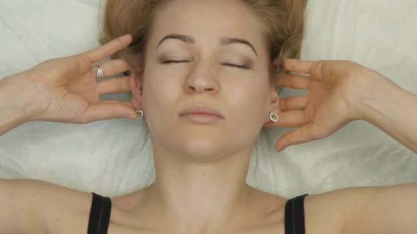 Masaje de cuello acostado en la cama. mujer rubia haciendo auto-masaje, masaje facial antienvejecimiento en casa — Vídeos de Stock