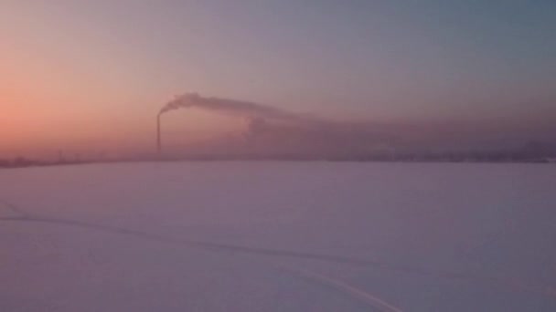 Volando sopra il tramonto campo di neve e solitario camino-gambo con fumo all'orizzonte — Video Stock