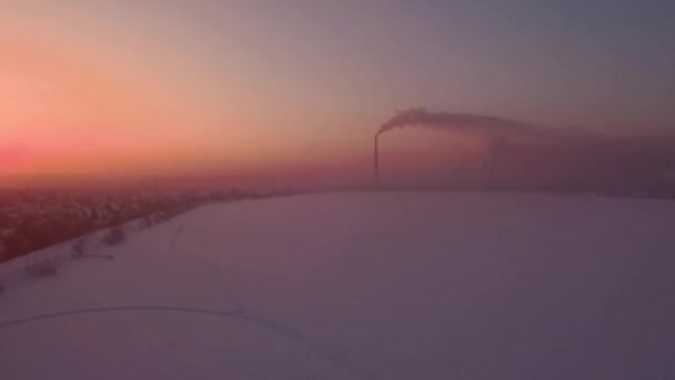 Volando sobre el atardecer del campo de nieve y solitaria chimenea-tallo con humo en el horizonte — Vídeo de stock