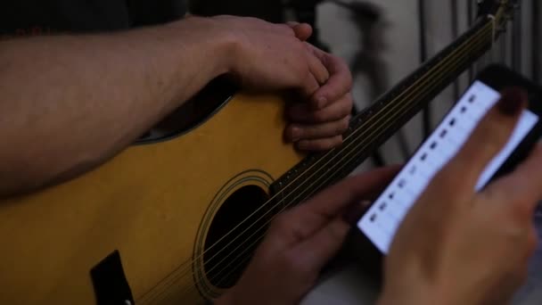 Tangan close-up berlatih dalam bermain gitar dan tangan dengan telepon. gerak lambat — Stok Video