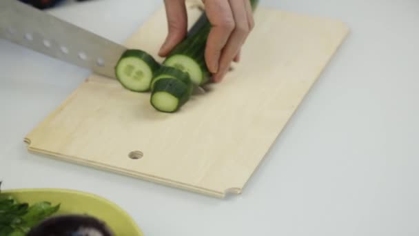 Snijden de komkommer voor sla. Snij groenten aan boord van de houten keuken. — Stockvideo