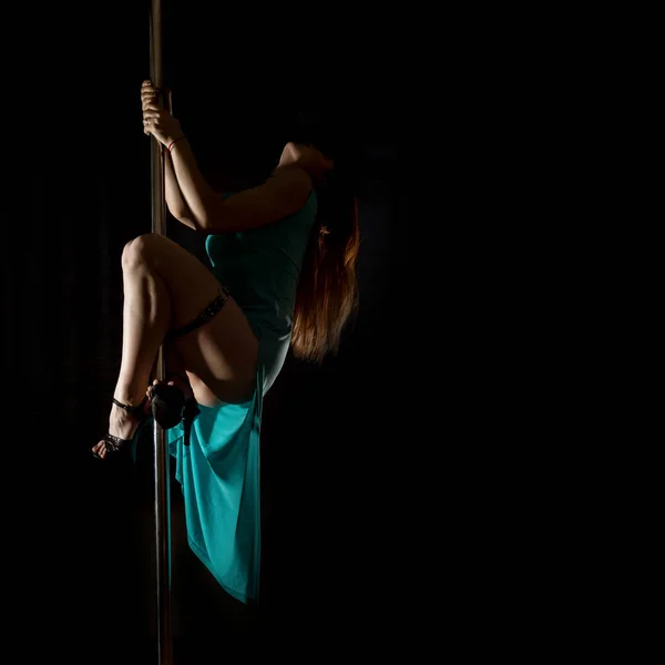 Striptease dansen met een paal in de nachtclub. Prachtige sexy vrouw in een lange turquoise jurk met een gleuf op een donkere achtergrond. vrije ruimte voor uw tekst — Stockfoto