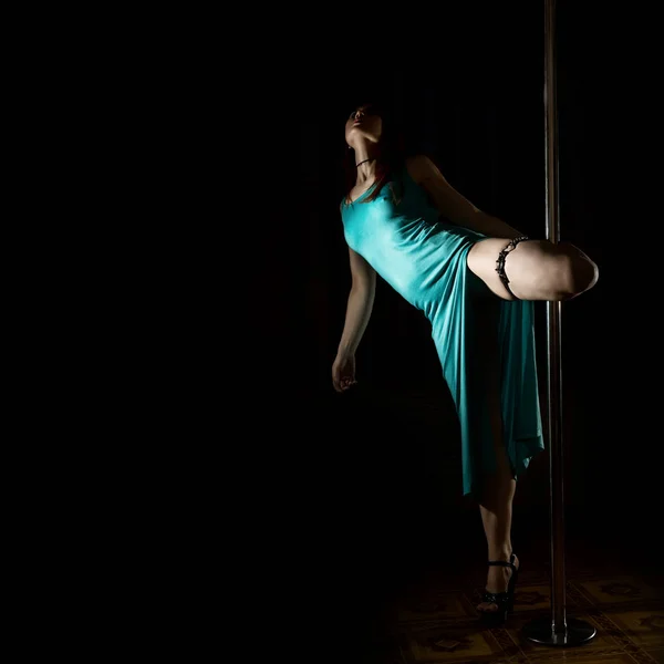 Στριπτιζ χοροί με έναν πόλο στο νυχτερινό κέντρο. Πανέμορφη σέξι γυναίκα σε ένα μακρύ τυρκουάζ φόρεμα με ένα σκίσιμο σε σκούρο φόντο. ελεύθερο χώρο για το κείμενό σας — Φωτογραφία Αρχείου