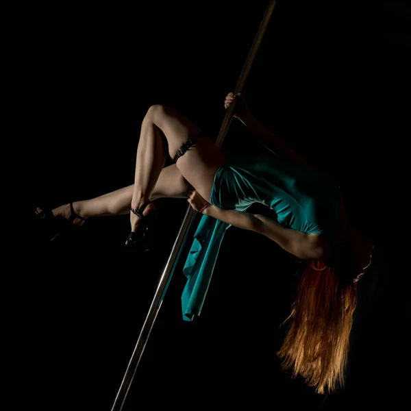 striptease dances with a pole in night club. Gorgeous sexy woman in a long turquoise dress with a slit on a dark background. free space for your text
