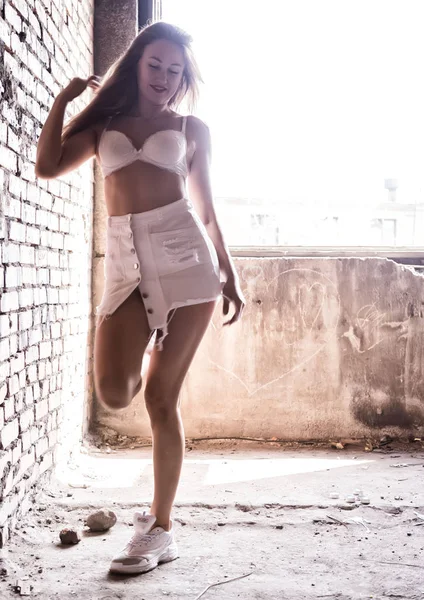 Σέξι νεαρή γυναίκα σε μια κοντή λευκή φούστα θέτοντας κοντά σε έναν τοίχο από τούβλα στο φως του ήλιου. θολή φως — Φωτογραφία Αρχείου