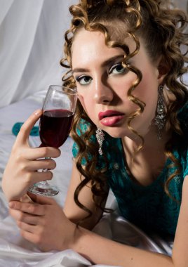 gizemli genç kıvırcık kadın yatakta istirahat ve kırmızı şarap içiyor