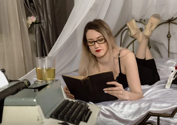 Mladá krásná žena s retro psací stroj. spisovatelky ležící na posteli a čte knihu — Stock fotografie