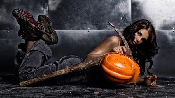 Beautiful tired sexy miner worker lies on a floor on steel background, pickaxe and orange helmet lies nearby