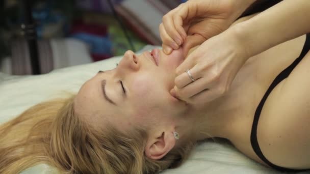 Блондинка делает самомассаж, массаж лица лежит в постели дома — стоковое видео
