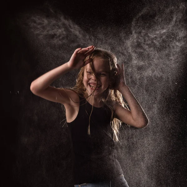 Junges Mädchen mit lebendigen Emotionen, das unter Wassertropfen tanzt. Kind planscht Wasser auf dunklem Hintergrund — Stockfoto